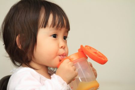 A baby drinking from an orange cup with a straw.