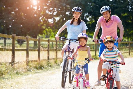 Two adults and two children wearing helmets while sitting on bikes on a dirt road.