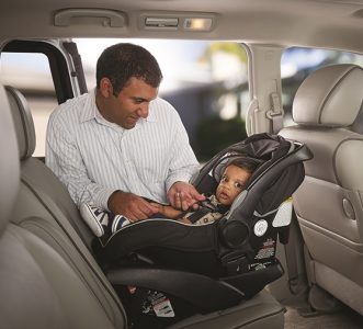 A parent smiling at their child who is buckled into a rear facing car seat.