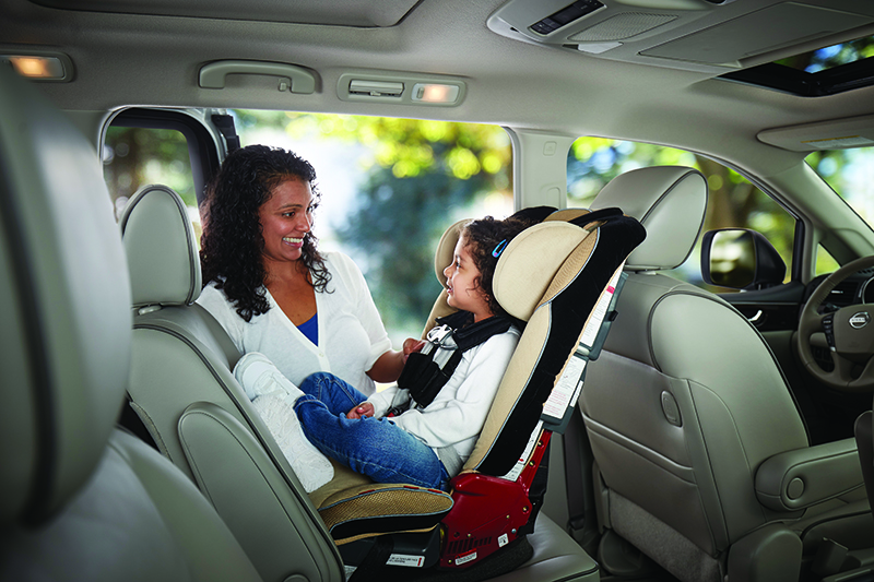 A parent smiling at their child who is buckled into a rear-facing car seat.