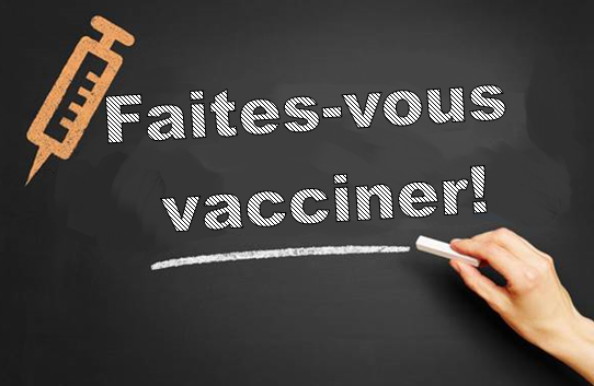 Tableau noir montrant le texte « Faites-vous vacciner! » écrit à la craie. Une illustration d’une seringue se trouve dans le coin supérieur gauche, et une main tenant un morceau de craie est visible à droite.