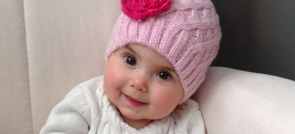 baby in pink hat and white onesie sitting in an arm chair