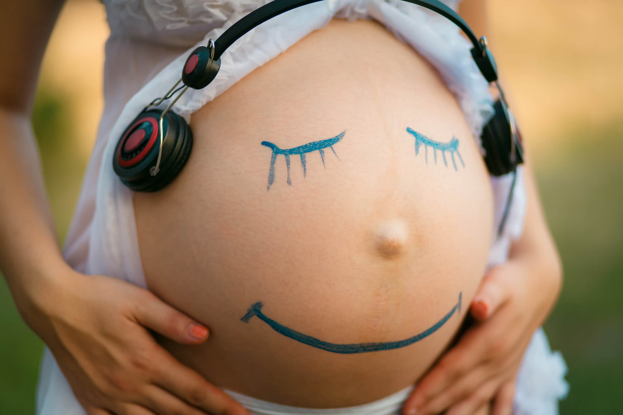 bare pregnant stomach with a smiley face drawn on it in blue