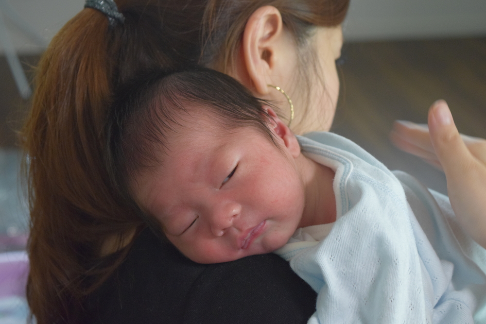 an adult holding a baby upright on their shoulder while burping them.