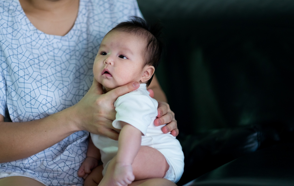 an adult holding a baby across their lap with the baby on their stomach.)