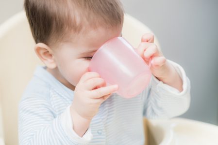 A baby holding a pink cup to their mouth.