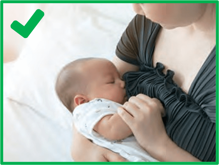 a baby in a white onesie being breastfed/chestfed with a green check mark in the top left corner