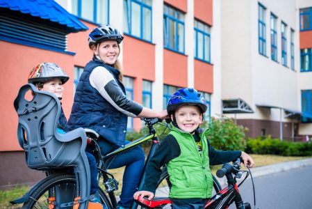 An adult and two children on bikes, one child in a carrier behind the adult, and an older child standing beside them.