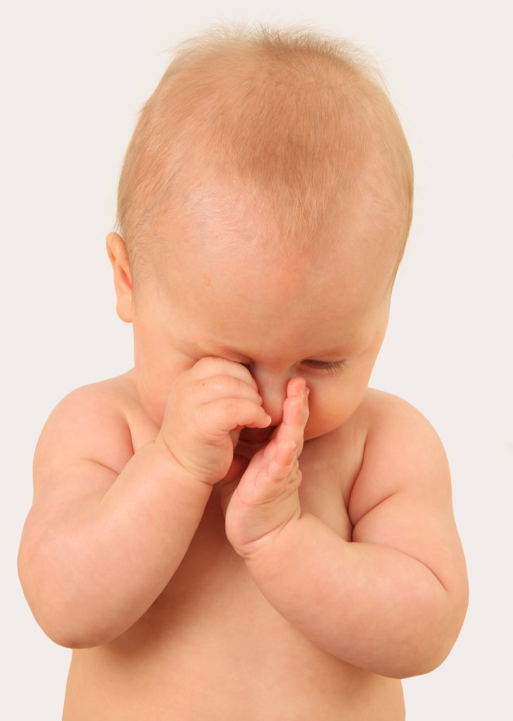 A baby with their head down and their hands over their eyes and nose