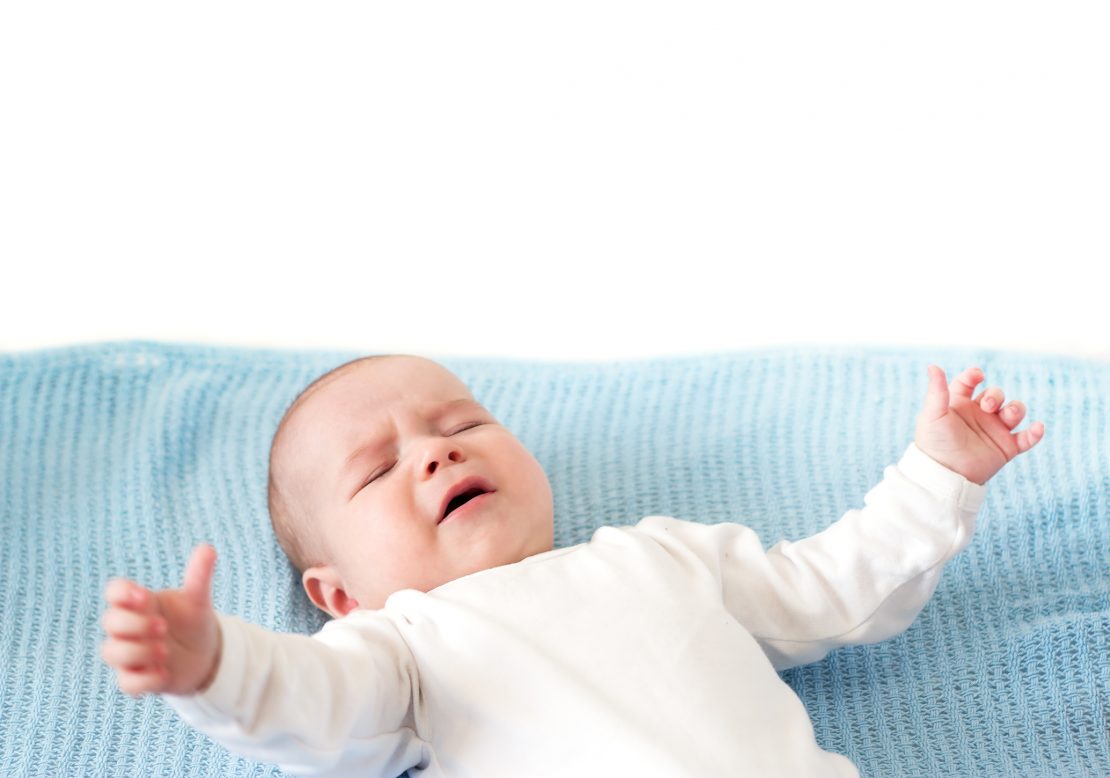 a crying baby lying down and reaching their arms out