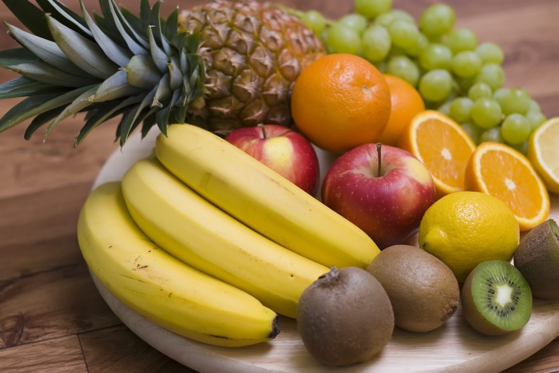Un arrangement de fruits comprenant des bananes, des ananas, des kiwis, des pommes, des oranges, des raisins et des citrons.