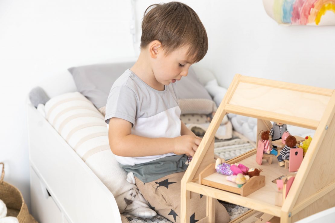 A child plays with a wooden dollhouse on a bed