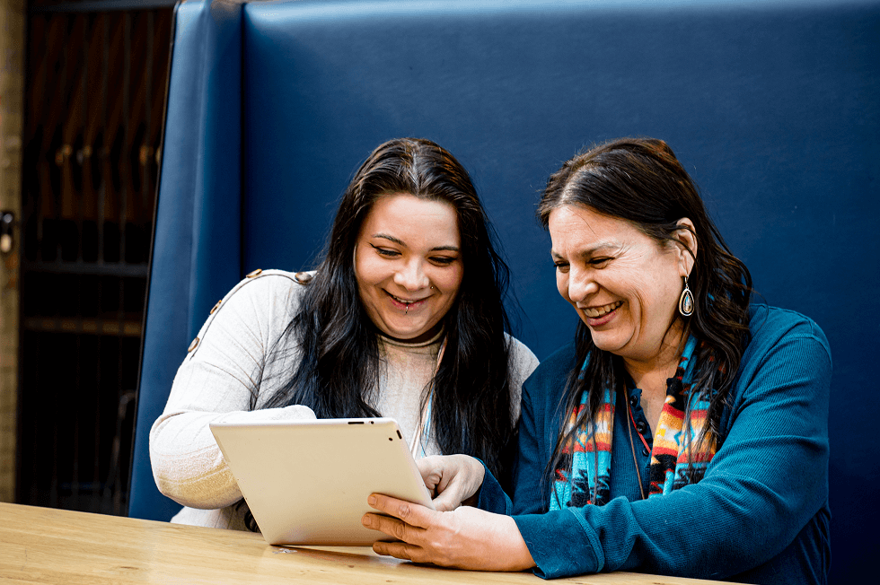 Two people smiling while looking at a tablet together.
