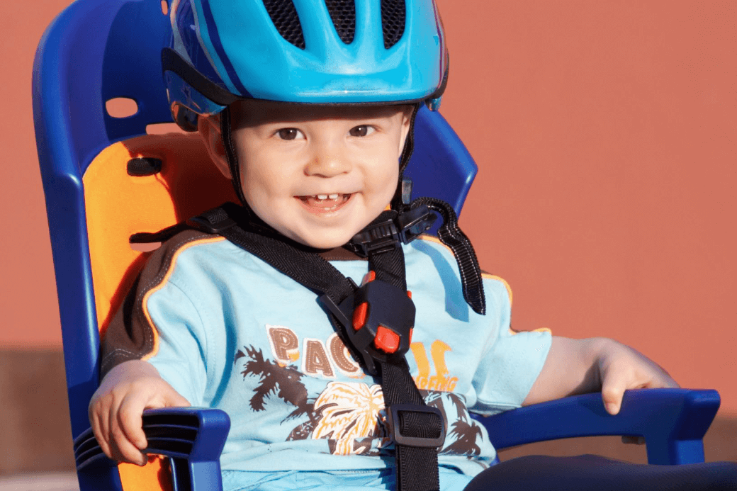 Un enfant portant un casque bleu est assis dans un siège bleu et orange.