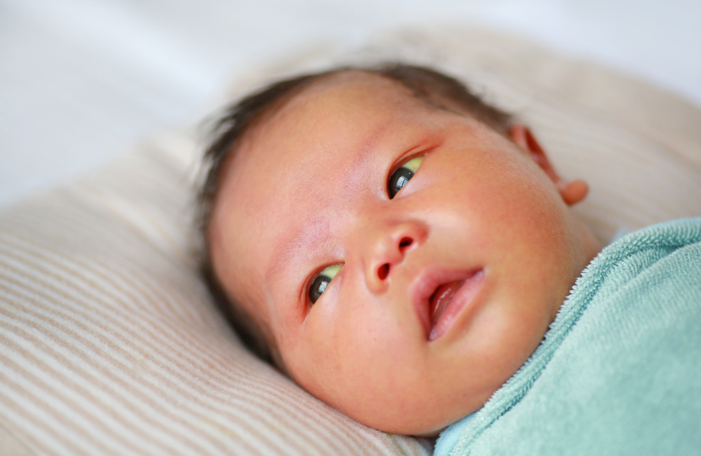 A baby lying on a striped pillow, wrapped in a light blue blanket.