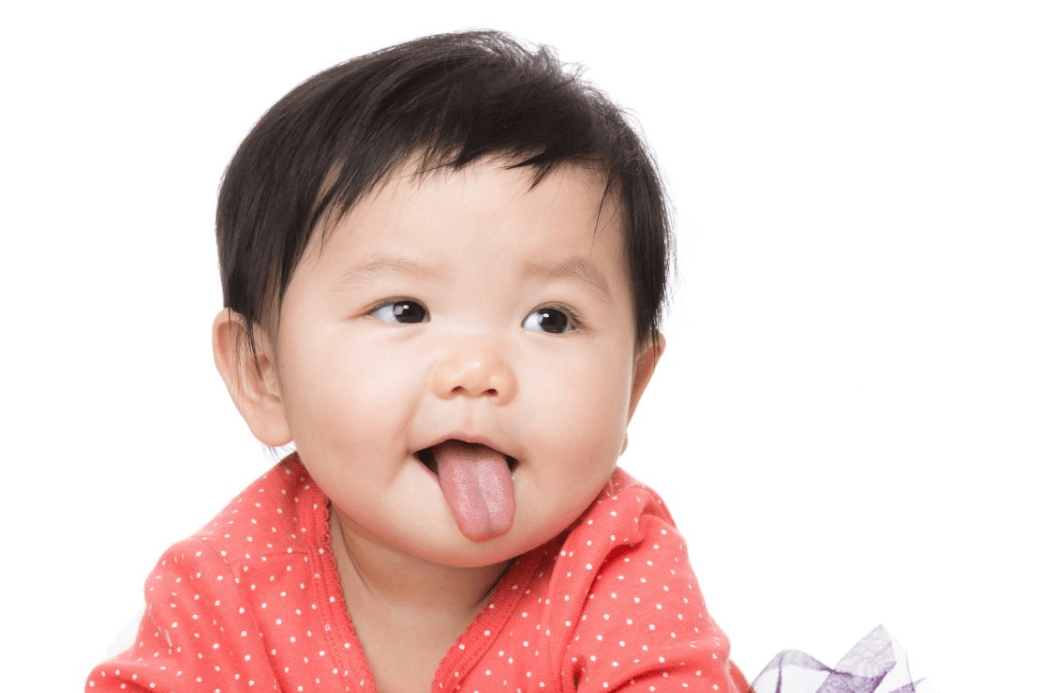 A young child in a red outfit with white polka dots, sticking their tongue out