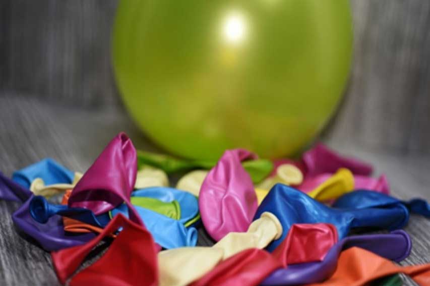 Uninflated latex balloons in the foreground with one yellow inflated balloon in the background.