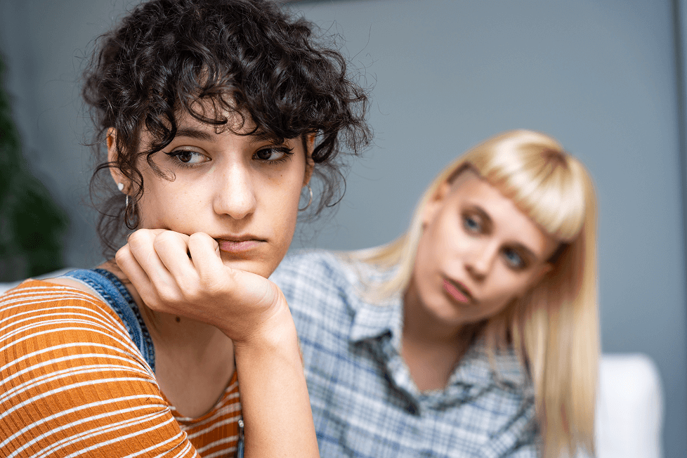 Person looking upset while another person sits behind them.