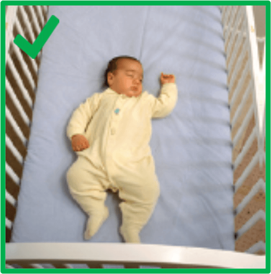  A baby is sleeping on their back on a blue mattress in a crib. There are no blankets, bumper pads or any other objects in the crib. There is a green border around the image and a green check mark in the top left corner.