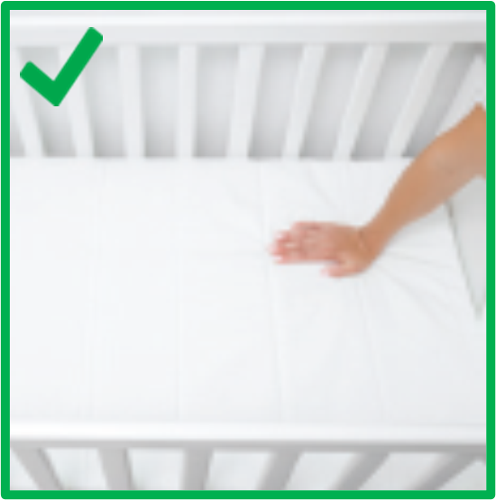 a hand touching a bare mattress in a crib. There are no blankets, bumper pads, toys or other objects in the crib. There is a green border around the image and a green check mark in the top left corner. 