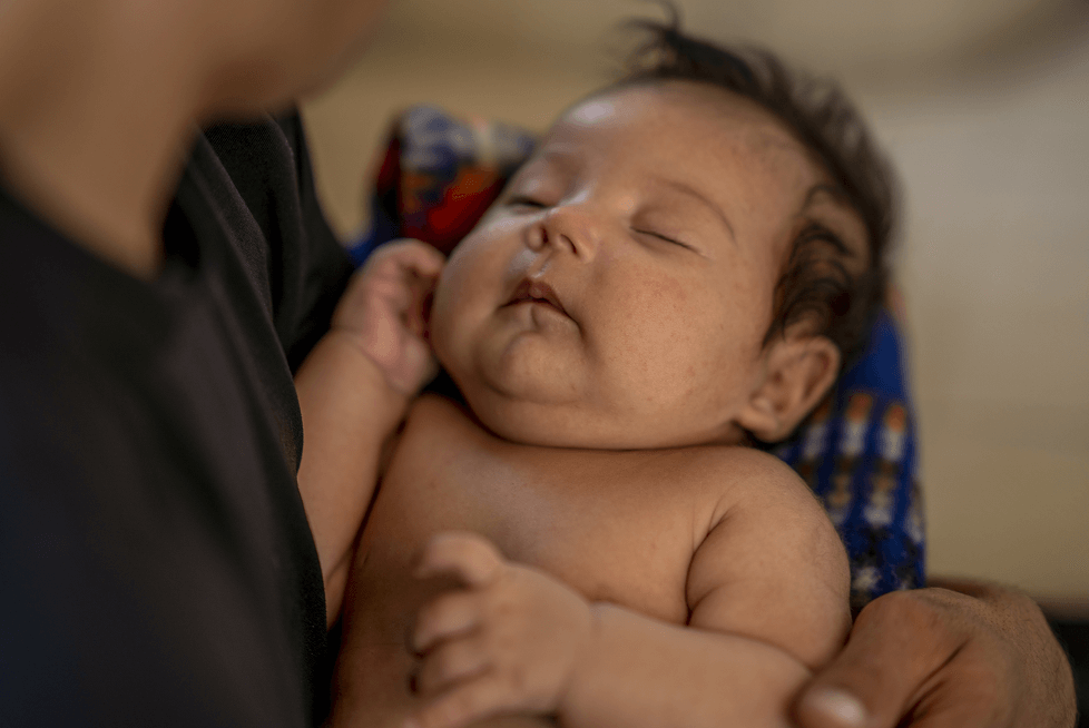 Infant sleeping peacefully while being held in the arms of an adult.
