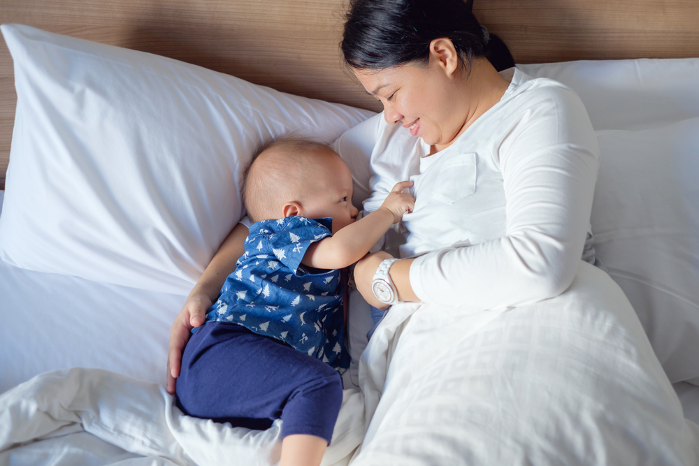 an adult lying in bed on their side while breastfeeding/chestfeeding their baby and demonstrating the below four points.