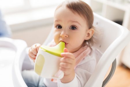A baby holding a green and white sippy cup to their mouth.