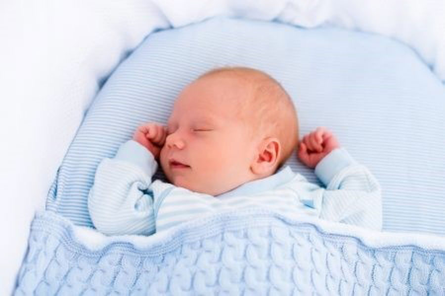 A baby lying on its back with a blanket covering it to its armpits and tucked into the sides of the crib