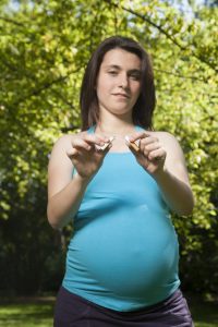 A pregnant person breaking a cigarette in half.