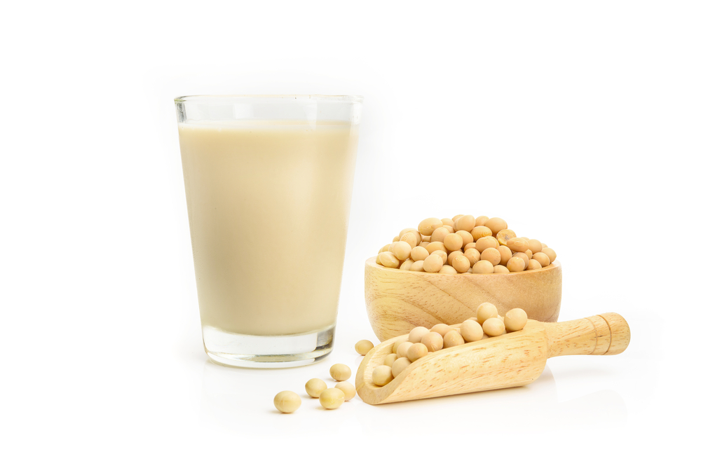  a glass of soy milk beside a small bowl and small scoop filled with soy beans.)