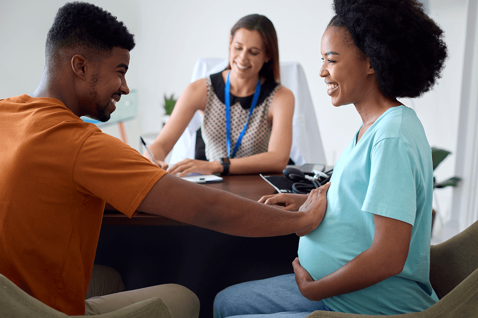 Pregnant couple at appointment with female doctor in office.