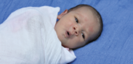 a baby on a blue sheet, swaddled in a white wrap