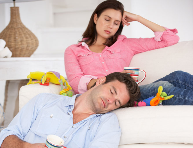 tired mom and dad resting on couch surrounded by toys