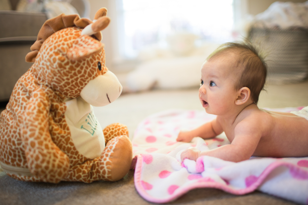 A baby lying on their tummy, looking up at a stuffed giraffe.