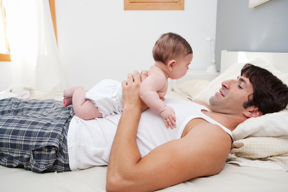 A baby doing tummy time while lying on an adult.