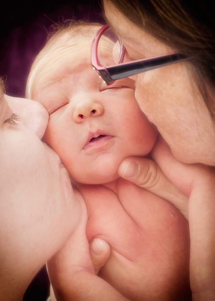 Two adults kissing the cheeks of a sleeping baby.
